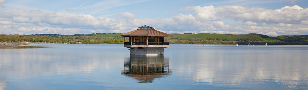 Carsington Water reservoir drain house on a still spring day with Wind Turbines visible in the background on the hills.